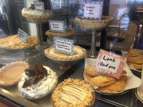 A display case filled with various pies, including peanut butter, chocolate, and fruit pies, all labeled.