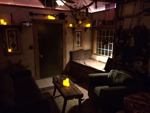 Cozy room with dim lighting, candles, and vintage decor, featuring a sofa, armchair, and a wooden coffee table.