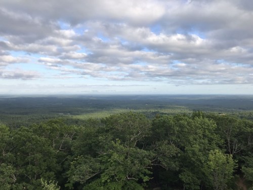 A panoramic view of lush green hills under a cloudy sky, stretching into the distance.