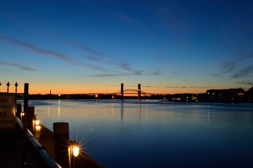 A serene river scene at dusk, featuring a bridge and reflections on the water under a colorful sky.