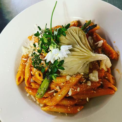 A plate of pasta with a creamy sauce, topped with flowers and herbs, garnished with an artichoke heart.