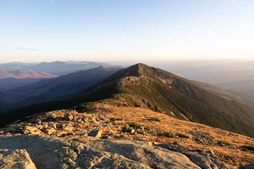 A scenic mountain landscape at sunset, showcasing rolling hills and a clear sky.