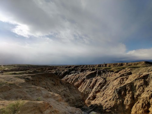 A vast, rugged landscape with layered rock formations under a cloudy sky.