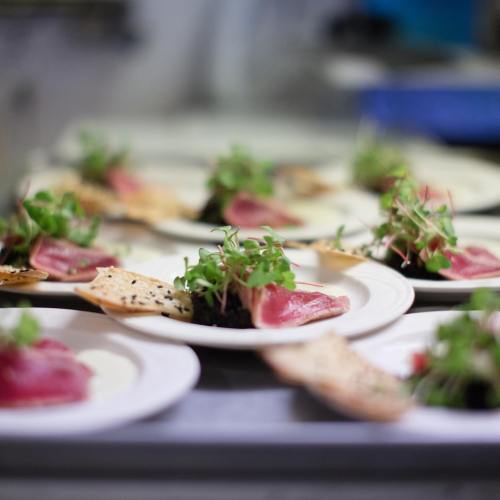 Plates of gourmet food featuring sliced meat, greens, and crispy crackers, arranged in a kitchen setting.