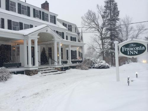 A snowy scene of the Franconia Inn, featuring a large white building and a sign, surrounded by winter landscapes.