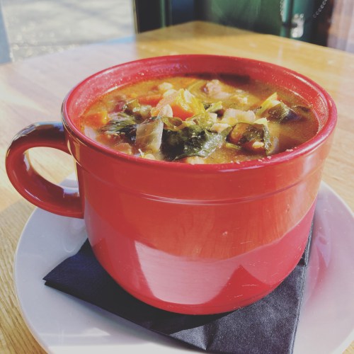 A vibrant red mug filled with hearty vegetable soup, resting on a black napkin on a wooden table.