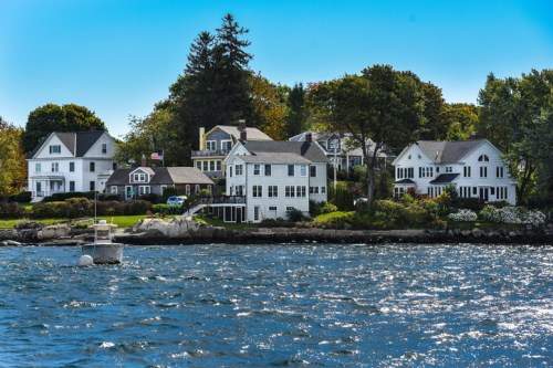 A scenic view of waterfront homes with trees, blue sky, and a small boat on the water.