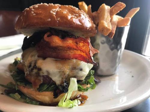 A juicy burger with bacon, melted cheese, and lettuce, served with a side of crispy fries on a white plate.