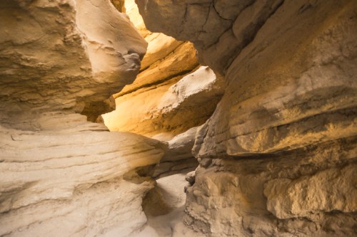 A narrow passageway between tall, layered rock formations illuminated by soft light.