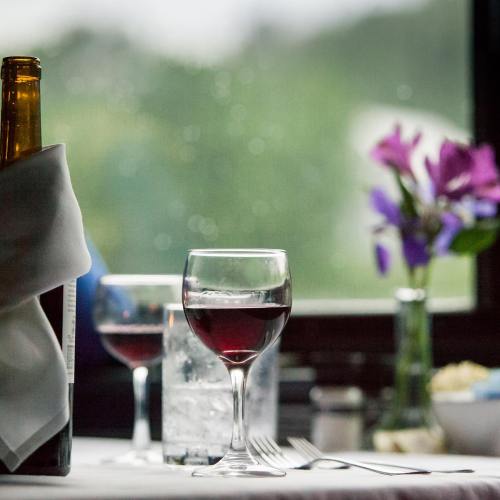 A table setting with a glass of red wine, a bottle, and a vase of purple flowers, with a blurred background.