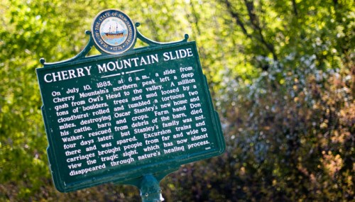 Historical marker about the Cherry Mountain Slide, detailing the event from July 10, 1885, in a natural setting.