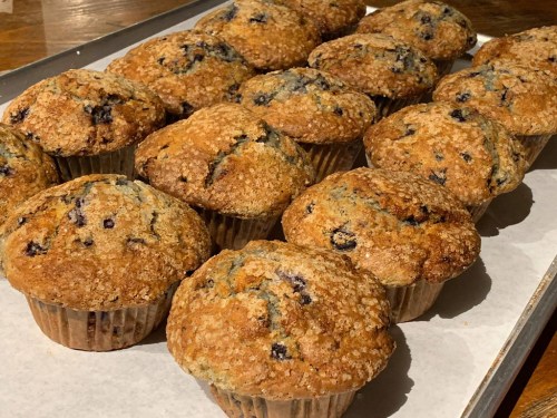 A tray of freshly baked blueberry muffins with a golden-brown crust and a sprinkle of sugar on top.