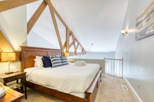 Cozy bedroom with a wooden bed, decorative pillows, and exposed beams, featuring soft lighting and a warm atmosphere.