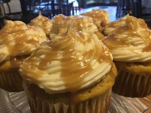 A close-up of cupcakes with creamy white frosting and a drizzle of caramel sauce on top.
