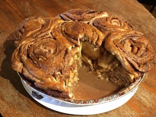 A freshly baked apple cinnamon roll pie with a slice removed, revealing its gooey filling, on a wooden table.
