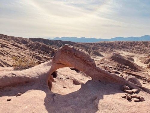 A natural rock arch in a rugged desert landscape with distant mountains under a clear sky.