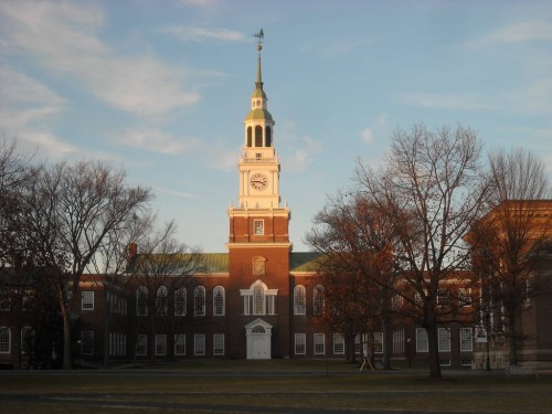 Historic building with a clock tower, surrounded by bare trees and a clear sky, bathed in warm sunlight.