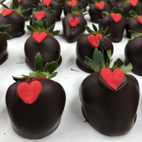 Chocolate-covered strawberries with red heart decorations, arranged neatly on a white surface.