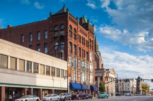 Historic brick buildings line a street under a blue sky with scattered clouds, showcasing architectural details.