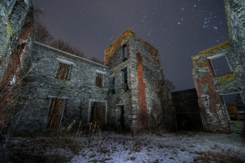 Ruins of a stone building under a starry night sky, with overgrown grass and a sense of abandonment.