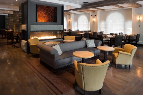 Cozy restaurant interior featuring a fireplace, gray sofa, yellow chairs, and wooden accents.