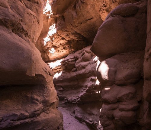 Narrow canyon with smooth, reddish rock walls and sunlight illuminating the path.