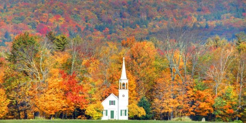 A white church with a steeple surrounded by vibrant autumn foliage in shades of orange, red, and yellow.