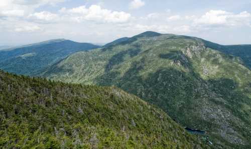 Aerial view of lush green mountains under a partly cloudy sky, showcasing rolling hills and dense forest.