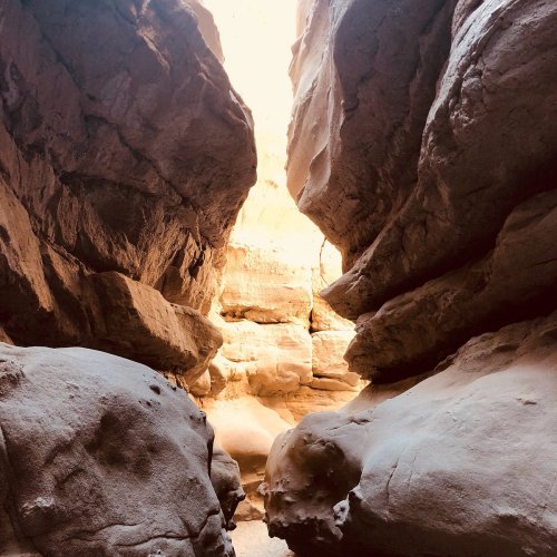 A narrow canyon with towering rock walls and a bright light at the end, creating a dramatic natural passageway.