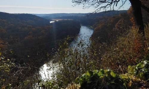 A scenic view of a winding river surrounded by autumn foliage and hills under a clear sky.