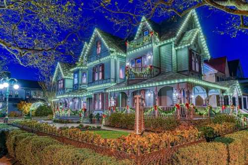 A beautifully decorated Victorian house illuminated with green lights and festive wreaths during the evening.