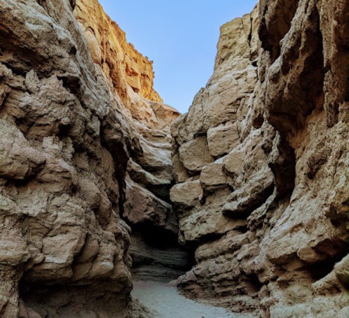 A narrow canyon with towering rock formations and a clear blue sky above.
