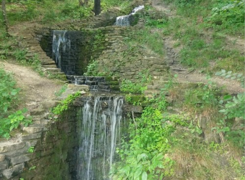 A serene stone waterfall cascading down a lush, green hillside surrounded by foliage.