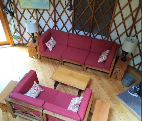Cozy yurt interior with red sofas, wooden furniture, and lamps, featuring a warm, inviting atmosphere.