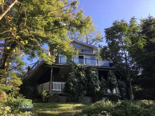 A two-story house on a raised platform, surrounded by trees and greenery under a clear blue sky.