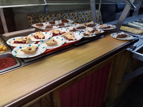 A buffet table displaying various desserts on plates, including pie and cake, with a colorful tablecloth in the background.