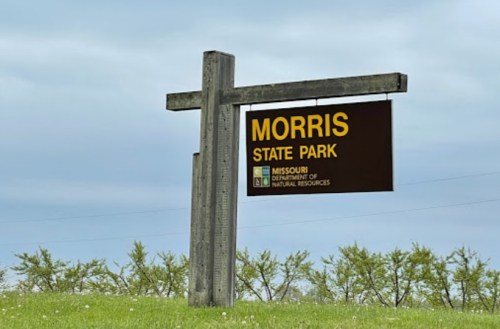 Sign for Morris State Park, Missouri, with a cloudy sky and green grass in the background.