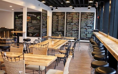 Interior of a restaurant featuring wooden tables, black chalkboard menus, and a mix of chairs and stools.