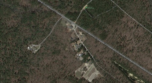 Aerial view of a wooded area with roads and scattered buildings, surrounded by dense forest.