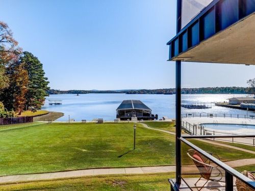Scenic view of a lake with a dock, grassy area, and swimming pool under a clear blue sky.