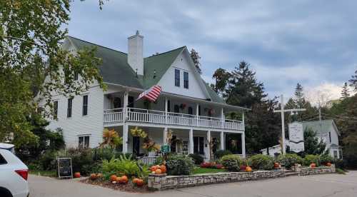 A charming white house with a green roof, decorated with pumpkins and flowers, under a cloudy sky. An American flag is displayed.