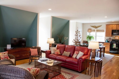 Cozy living room with red leather sofa, wooden furniture, and a TV, featuring green accent walls and natural light.