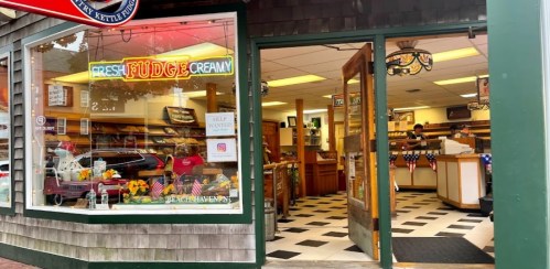 A cozy shop entrance with a "Fresh Fudge" sign, showcasing a warm interior filled with baked goods and decorations.