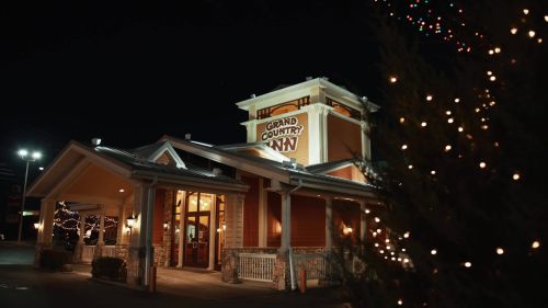Exterior of Grand Country Inn at night, decorated with festive lights and surrounded by trees.