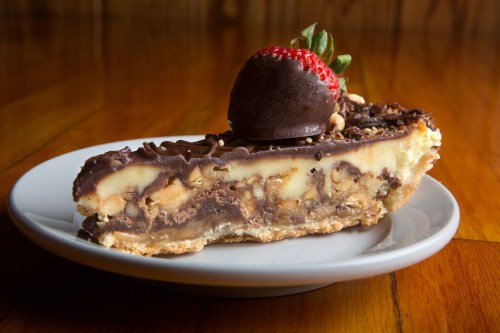 A slice of chocolate and nut pie topped with a chocolate-covered strawberry, served on a white plate.