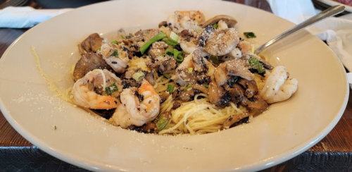 A bowl of pasta topped with shrimp, mushrooms, and green onions, garnished with cheese.