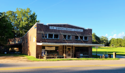 Historic brick building with "The Simmons-Wright Company" sign, surrounded by trees and a clear blue sky.
