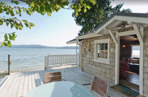 Cozy lakeside cabin with a wooden deck, surrounded by trees and a view of the water.