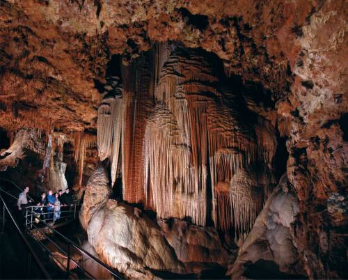 Visitors explore a stunning cave with impressive stalactites and stalagmites, illuminated by soft lighting.