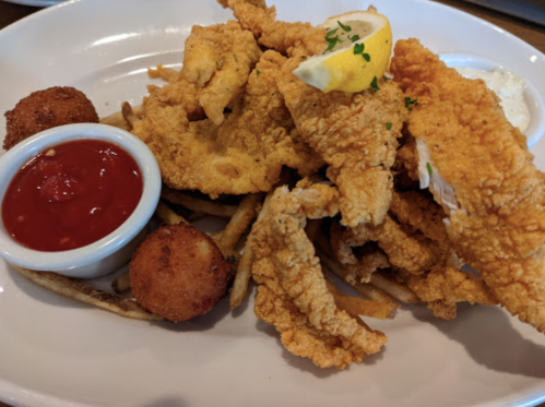 A plate of fried fish fillets with a lemon wedge, served with hushpuppies and dipping sauce.